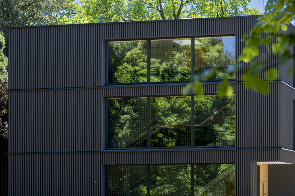 Dunkle Fassade des Hauses August im Seegut Zeppelin mit großen Fenstern zwischen Bäumen