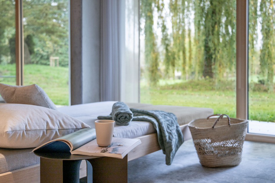 Ruheraum im Garten Spa des Seegut Zeppelin mit Liege, Handtuch, Kaffeetasse und bodentiefen Fenstern ins Grüne
