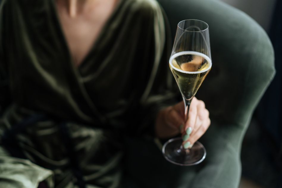Gast im grünen Samtkleid mit einem Glas Champagner zum Jahreswechsel