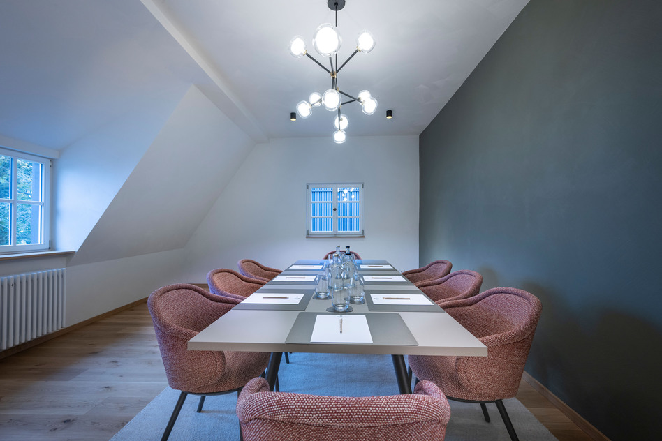 Tagungsraum in der Villa Gminder des Seegut Zeppelin mit Dachschräge, Tisch, gepolsterten Stühlen und Kronleuchter