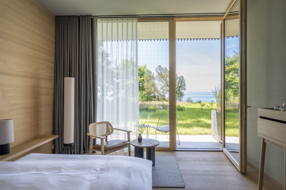 Waldzimmer im Seegut Zeppelin mit Bett, bodentiefen Fenstern und Terrasse mit Blick auf Wiese und Bodensee
